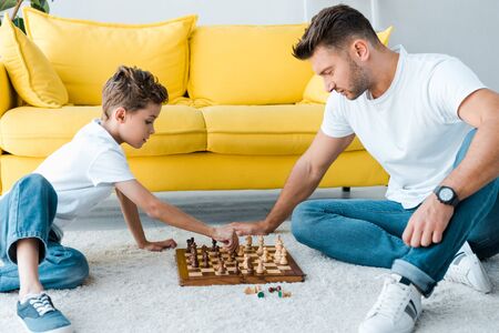side view of handsome father and son playing chess on carpetの写真素材