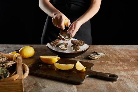 cropped view of woman squeezing lemon on oyster isolated on blackの写真素材