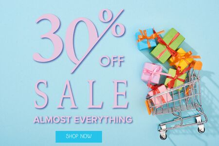 top view of festive wrapped presents in shopping cart on blue background with 30 percent off sale...