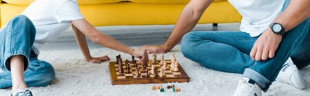 panoramic shot of father and son playing chess on carpet