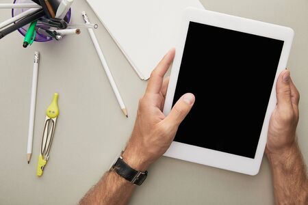 top view of man holding digital tablet near notebook, glasses and stationery isolated on grey