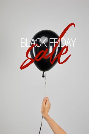cropped view of woman holding  black balloon isolated on grey with black Friday sale illustrationの写真素材