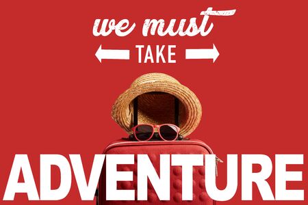 red colorful travel bag with straw hat and sunglasses isolated on red with we must take adventure illustrationの写真素材