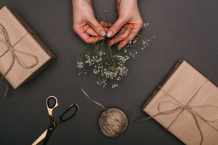 cropped view of woman packing gift boxes with craft paper, twine and flowers on blackの写真素材
