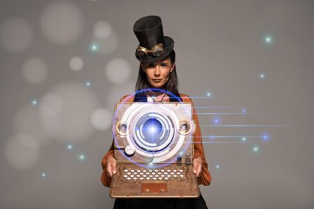 steampunk woman in top hat with goggles showing vintage laptop with glowing digital illustration isolated on greyの写真素材