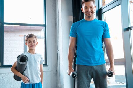 happy father holding dumbbells near cute son with fitness matの写真素材
