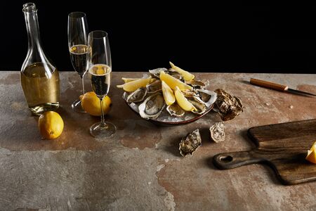champagne glasses with sparkling wine near bottle, oysters and lemons in bowl isolated on blackの写真素材