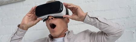 Shocked man in virtual reality headset playing video game, panoramic shot