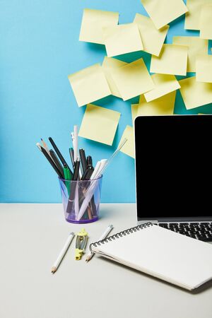 laptop with blank screen near sticky notes, glasses and stationery on blue and whiteの写真素材