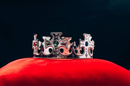 ancient silver crown with gemstones on red pillow, isolated on blackの写真素材