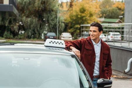 Smiling taxi driver looking at away beside car