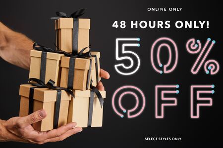 cropped view of man holding cardboard gift boxes with ribbons isolated on black with 48 hours 50...