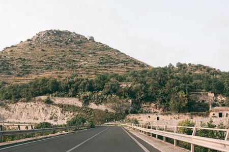 asphalt road near green trees on hill in ragusa, italy