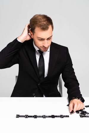 pensive and handsome businessman in suit playing domino isolated on greyの写真素材