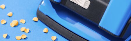 panoramic shot of holepunch with paper circles on blue background