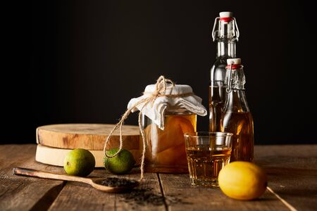 glass jar with kombucha near lime, lemon, spice and bottles on wooden table isolated on blackの写真素材