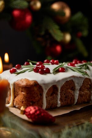 selective focus of traditional Christmas cake with cranberry near burning candles, Christmas wreath with baubles on wooden tableの写真素材