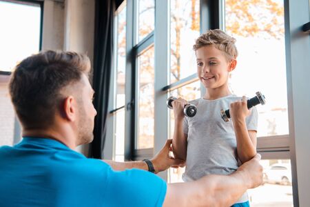 selective focus of happy father touching cute son weightlifting dumbbells