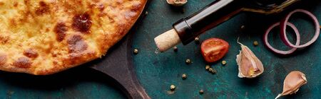 Imereti khachapuri with wine bottle and vegetables on textured green background, panoramic shotの写真素材