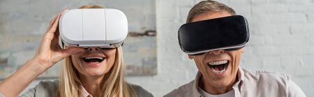 Panoramic shot of laughing couple in virtual reality headsets at home