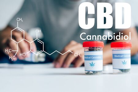 selective focus of bottles with medical cannabis on table with man on background with cbd molecule...