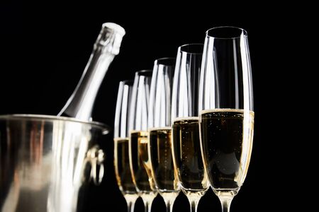 selective focus of champagne glasses with sparkling wine near ice bucket with bottle isolated on blackの写真素材