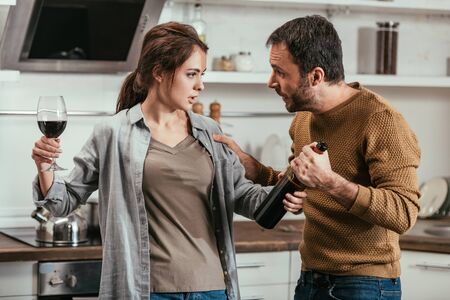 Woman holding wine and quarreling with husband on kitchenの写真素材