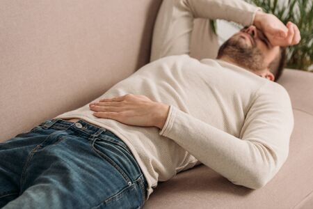 selective focus of man lying on sofa and suffering from headacheの写真素材