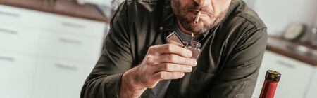 Cropped view of man lighting cigarette beside wine bottle, panoramic shot