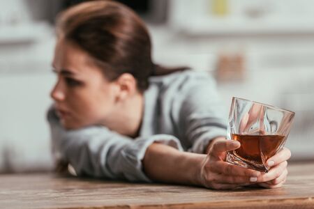 Selective focus of sad woman holding whiskey glass at tableの写真素材