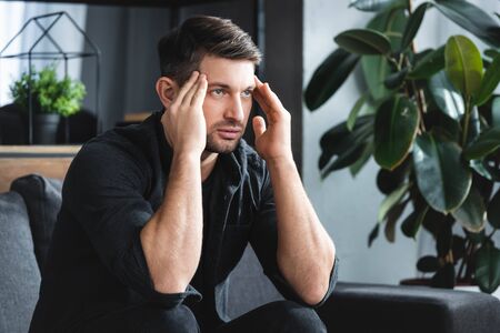 handsome man in shirt with headache touching head in apartment