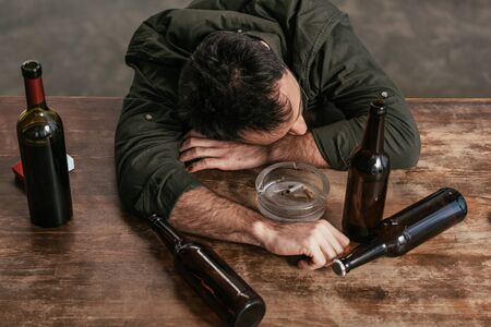 High angle view of drunk man lying on table with bottles and ashtrayの写真素材