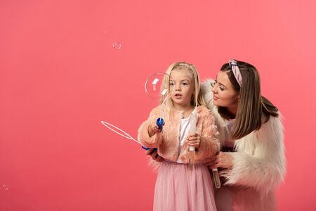 daughter and smiling mother blowing soap bubbles isolated on pinkの写真素材
