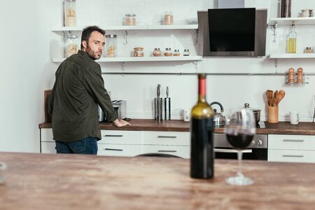 Selective focus of pensive man looking at wine on kitchen tableの写真素材