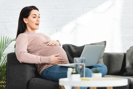 attractive pregnant woman having online consultation with doctor on laptop at home