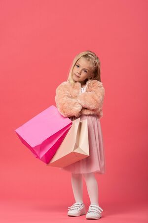 cute kid with crossed arms holding shopping bags on pink backgroundの写真素材