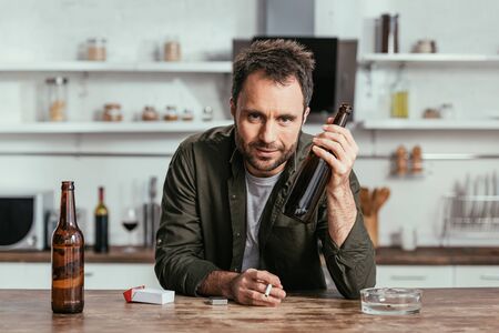 Alcohol addicted man with cigarette holding beer bottle and looking at camera