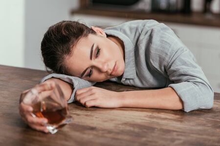 Selective focus of sadness woman holding whiskey glass at tableの写真素材