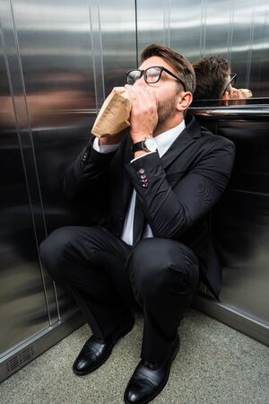 scared businessman in suit with claustrophobia breathing in paper bag in elevatorの写真素材