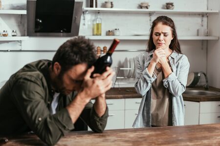 Selective focus of stressed woman and alcohol depended man with wine bottle on kitchenの写真素材