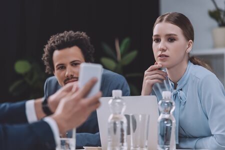 cropped view of businessman showing smartphone to multicultural colleaguesの写真素材