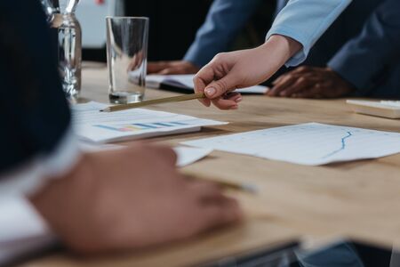 cropped view of businesswoman pointing with pencil at document during business meeting with...
