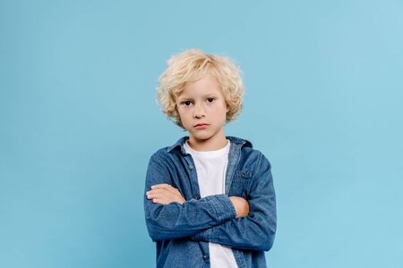 sad and cute kid with crossed arms looking at camera isolated on blue