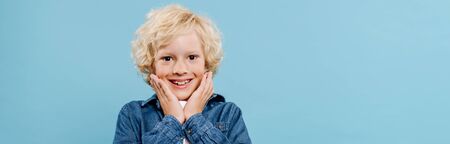 panoramic shot of smiling and shocked kid looking at camera isolated on blue