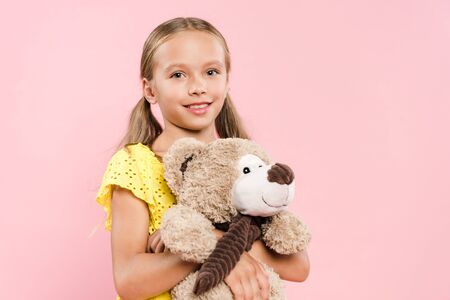 smiling kid looking at camera and holding teddy bear isolated on pinkの写真素材