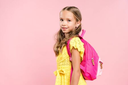 smiling schoolgirl with backpack looking at camera isolated on pinkの写真素材