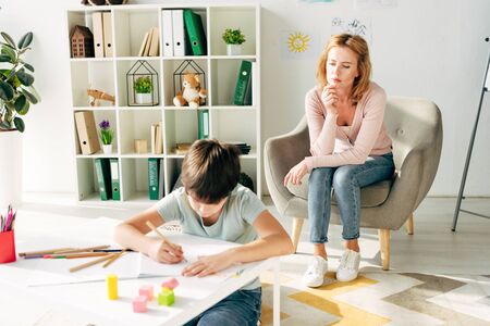 kid with dyslexia painting with pencil and child psychologist looking at him