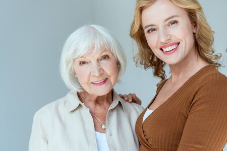 smiling daughter hugging mother and looking at camera isolated on greyの写真素材