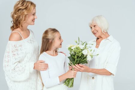 smiling granddaughter giving bouquet to grandmother isolated on greyの写真素材