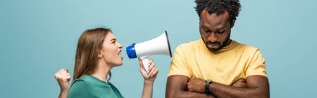 angry girl screaming in megaphone at african american boyfriend with crossed arms on blue background